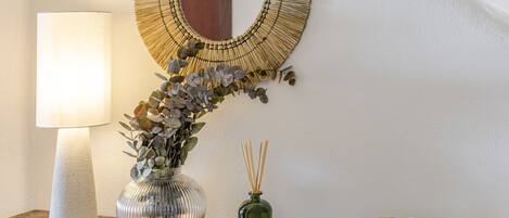 A lamp, a vase with plants, a reed diffuser, and a bowl on a wooden surface.