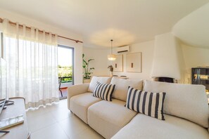 A modern living room with a beige sofa, striped pillows, a dining table, and a large window with sheer curtains. - S o Rafael Apartment by Minhos Guest (Albufeira)