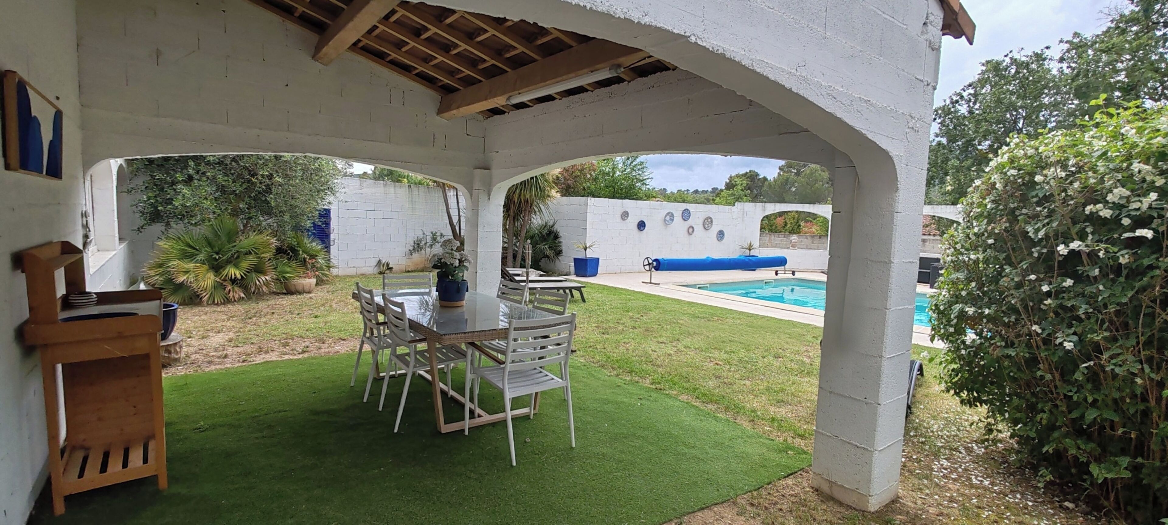 A covered patio with a table and chairs, a small pool, and a white wall with decorative plates.