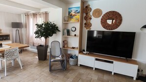 En moderne stue med et fladskærms-tv, et spiseområde med et træbord og stole, en potteplante og dekorativ vægkunst.