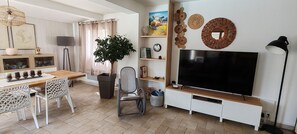 Ein modernes Wohnzimmer mit Flachbildfernseher, Essbereich mit Holztisch und Stühlen, einer Topfpflanze und Wanddekoration.