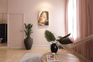 Ein Zimmer mit einem runden Holztisch, einer Zeitschrift, einer Pflanze in einer Vase, einer Hängematte und einem Bild an der Wand.