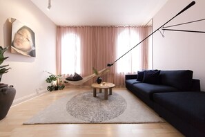 Ein Wohnzimmer mit einem dunklen Sofa, einem runden Couchtisch, einer Hängematte und einem großen Gemälde an der Wand.