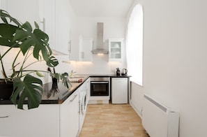 Eine schmale Küche mit weißen Schränken, einem eingebauten Backofen, einem Geschirrspüler und einem Fenster, das für natürliches Licht sorgt.