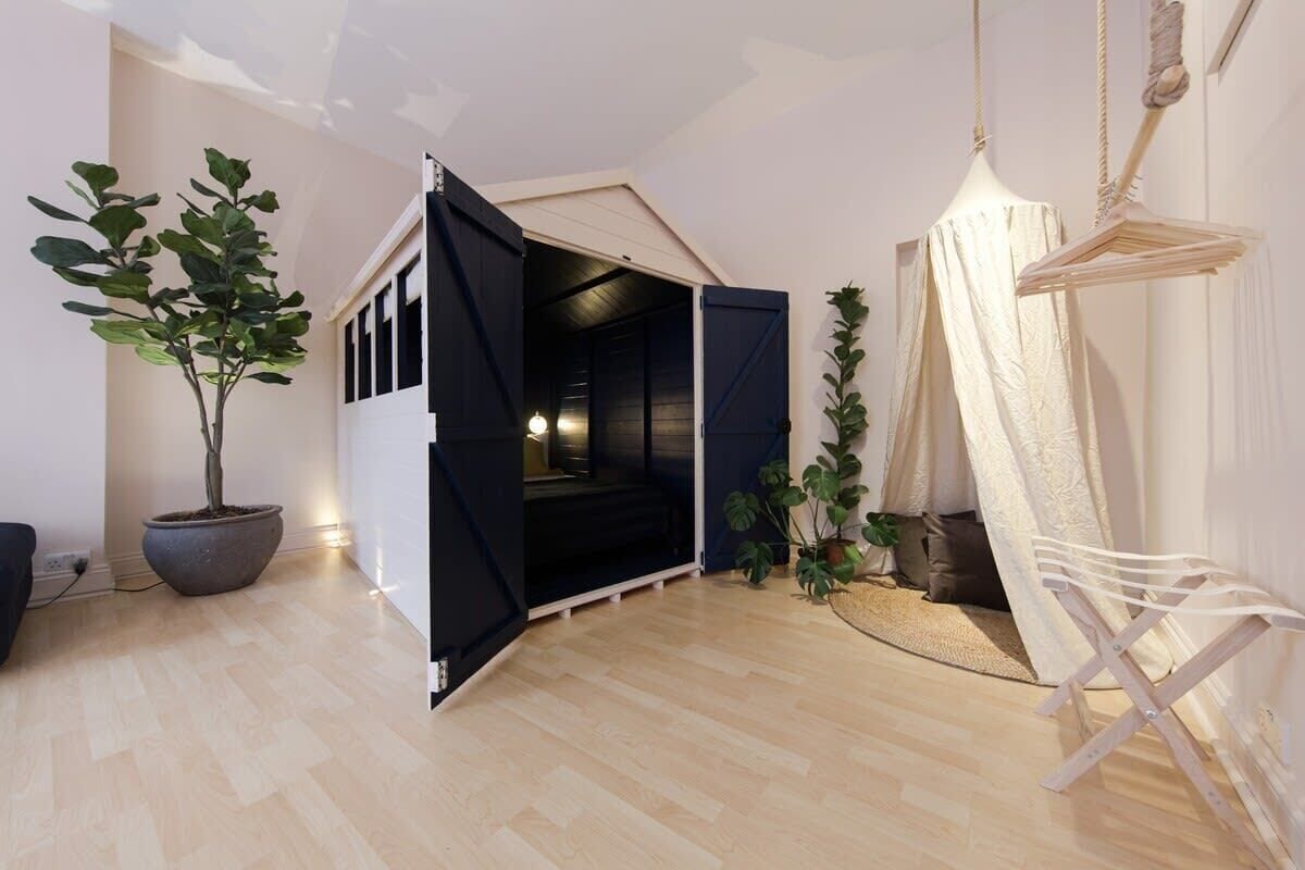 A room with a wooden floor, a potted plant, a hanging chair, and a tent-like structure with a door.