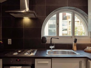 A modern kitchen with a gas stove, stainless steel sink, and a window with a view of buildings. - Grand 2BR Penthouse with 100" Cinema, Hyde Park (London)