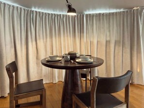 A round table with plates, cups, and a teapot, surrounded by chairs, with a lamp above and curtains in the background. - Grand 2BR Penthouse with 100" Cinema, Hyde Park (London)