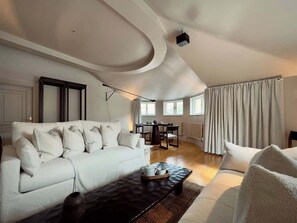 A modern living room with a white sofa, a dark coffee table, and a dining area with a table and chairs. - Grand 2BR Penthouse with 100" Cinema, Hyde Park (London)