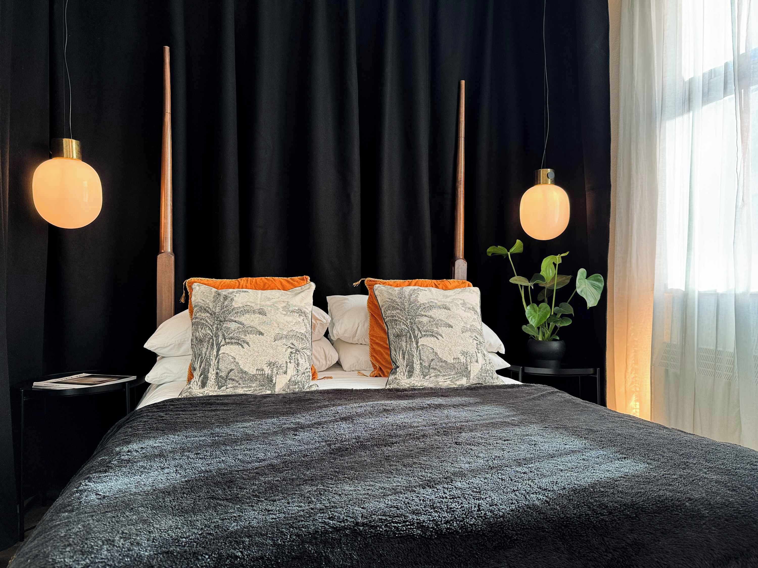 A bed with two pillows, a black headboard, and two hanging pendant lights.