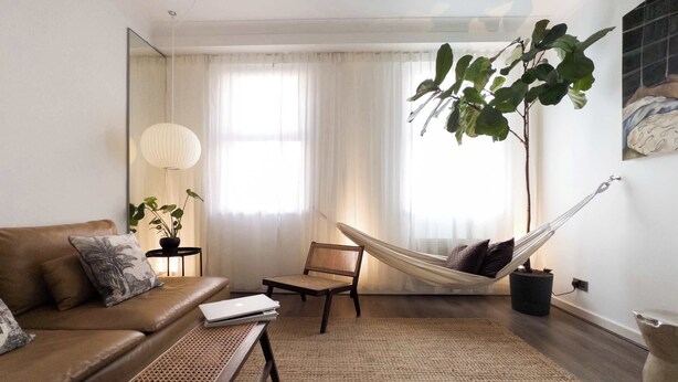 Ein Wohnzimmer mit einer Couch, einem kleinen Tisch, einem Sessel, einer Hängematte und einer großen Pflanze.