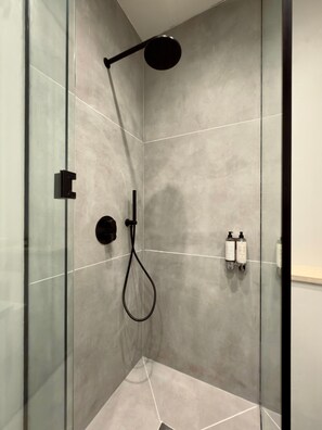 Une douche moderne dotée d’un pommeau de douche à main, d’un panneau de commande mural et de deux bouteilles de shampoing.