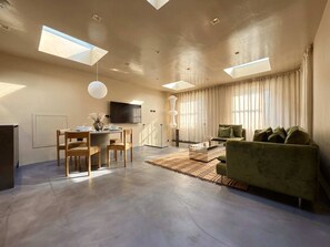Ein modernes Wohnzimmer mit Essbereich, einer Couch, einem Fernseher und einem großen Fenster.
