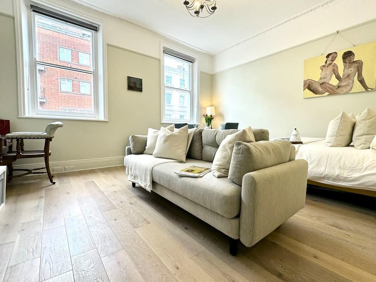 A room with a sofa, a chair, a bed, and a painting on the wall.