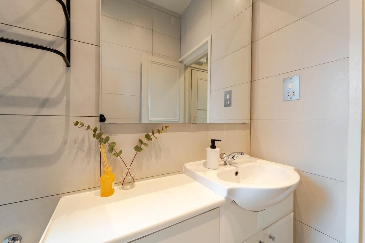 A modern bathroom with a white sink, mirror, and a small plant on the counter.