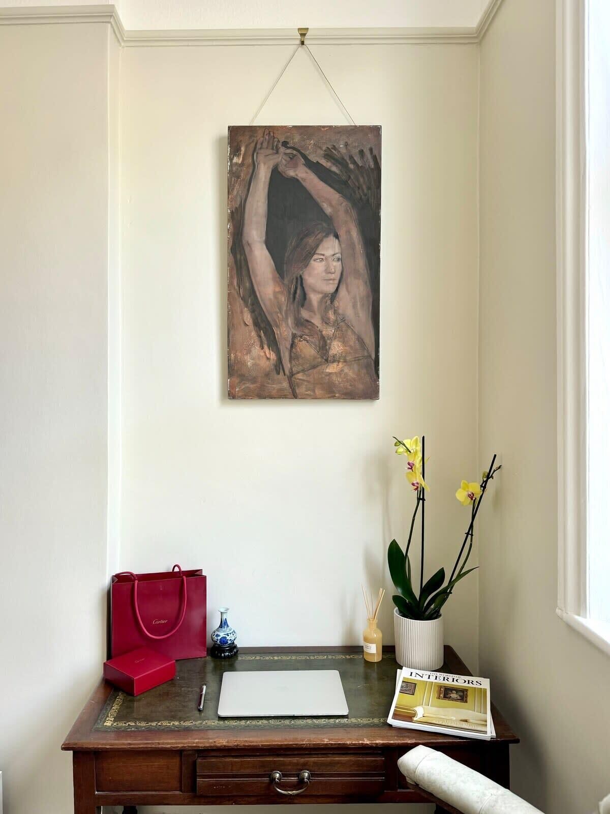 A desk with a red bag, a white vase with yellow flowers, a magazine, and a painting on the wall.