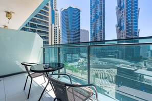 Ein Balkon mit Glastrennwand, einem runden Tisch und zwei Stühlen mit Blick auf eine Stadtlandschaft und moderne Hochhäuser.