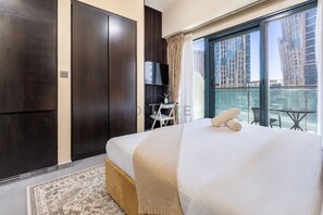 Ein Hotelzimmer mit einem großen Bett, einem Fernseher, einem kleinen Tisch und einem Balkon mit Blick auf die Stadt.
