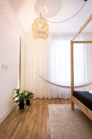 Ein Schlafzimmer mit einem hölzernen Bett, einer Hängematte, einer Pendelleuchte und Topfpflanzen.