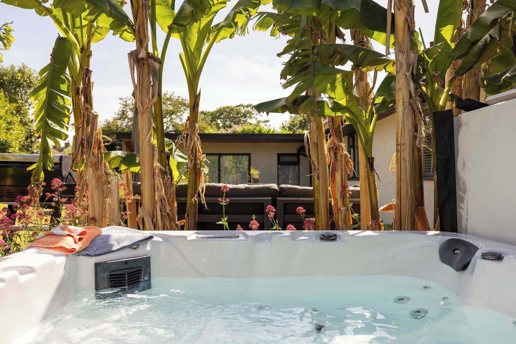 A hot tub surrounded by banana trees and a wooden fence.