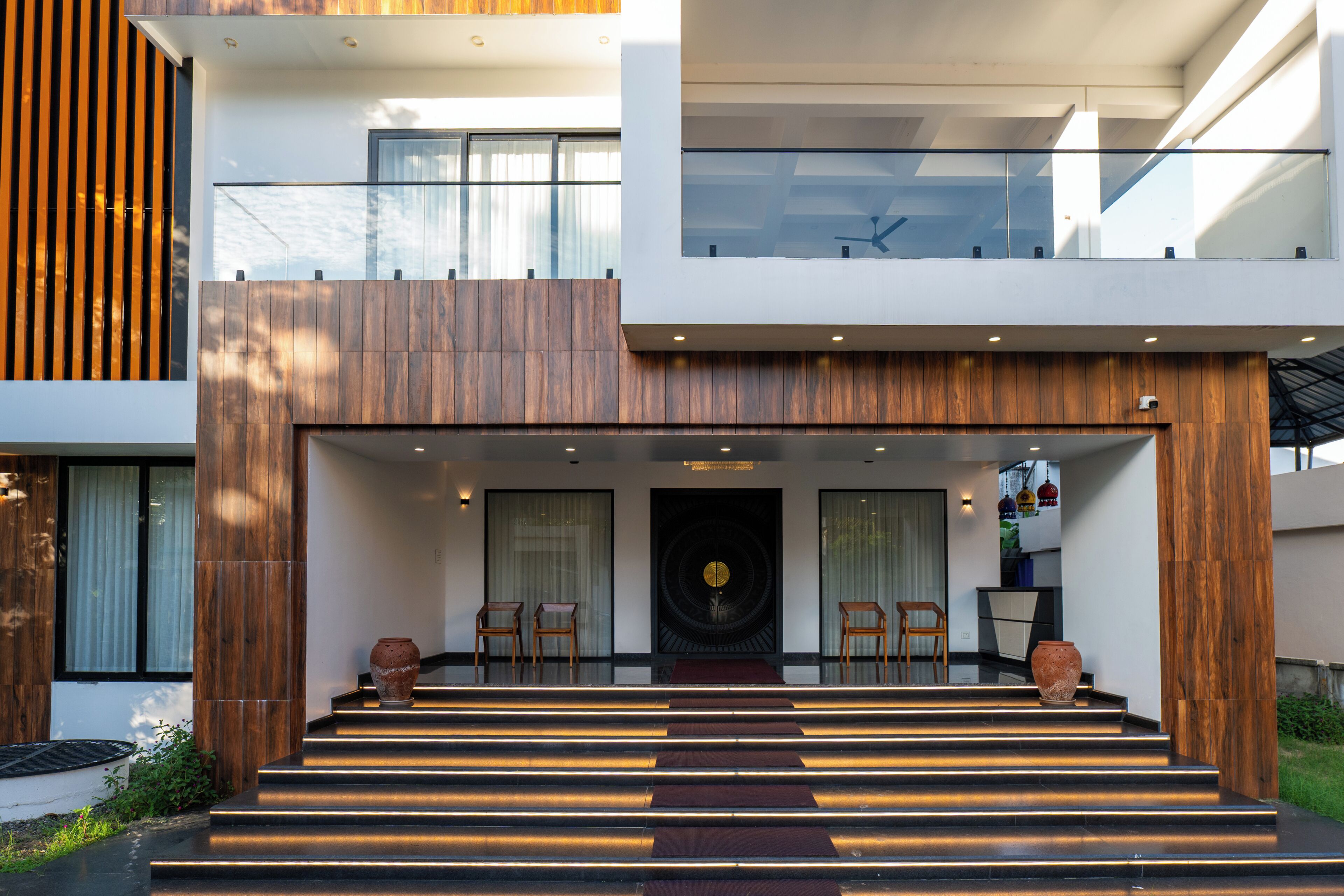 A modern building with a wooden facade, a set of stairs leading to a door, and a small seating area with chairs and a table.