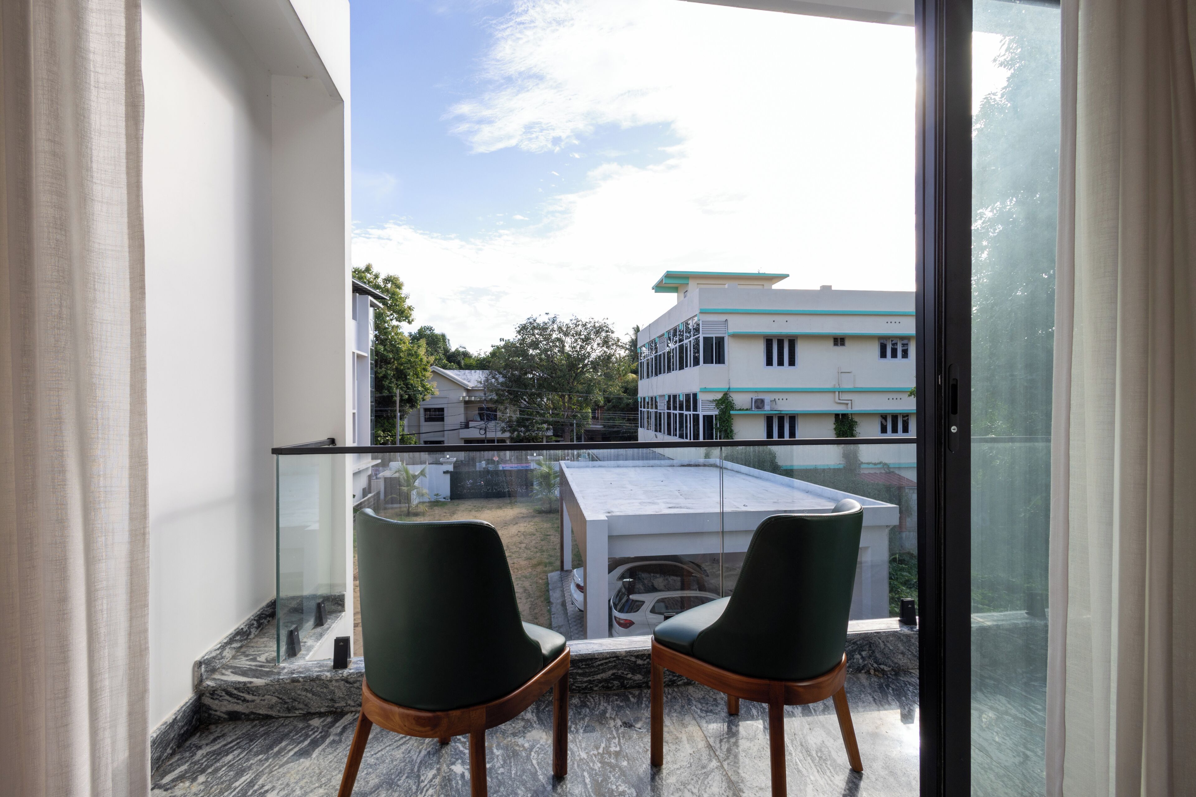 A balcony with two chairs, a glass railing, and a view of buildings and trees.