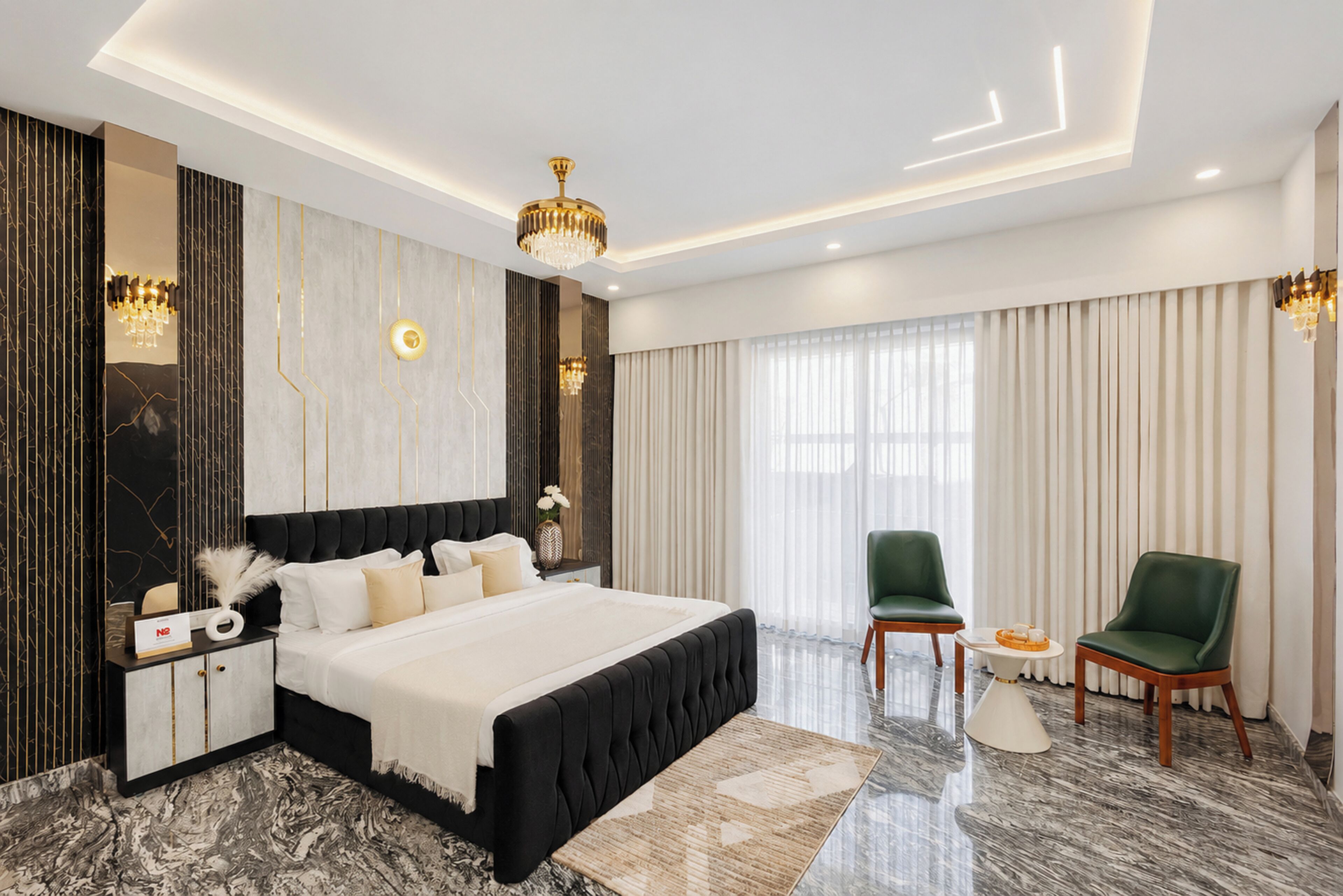 A modern hotel room with a large bed, a desk, two chairs, a chandelier, and a large window with curtains.