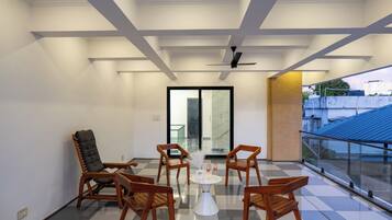 Un balcón moderno con piso a cuadros, barandilla de vidrio y un conjunto de sillas de madera y una mesa.