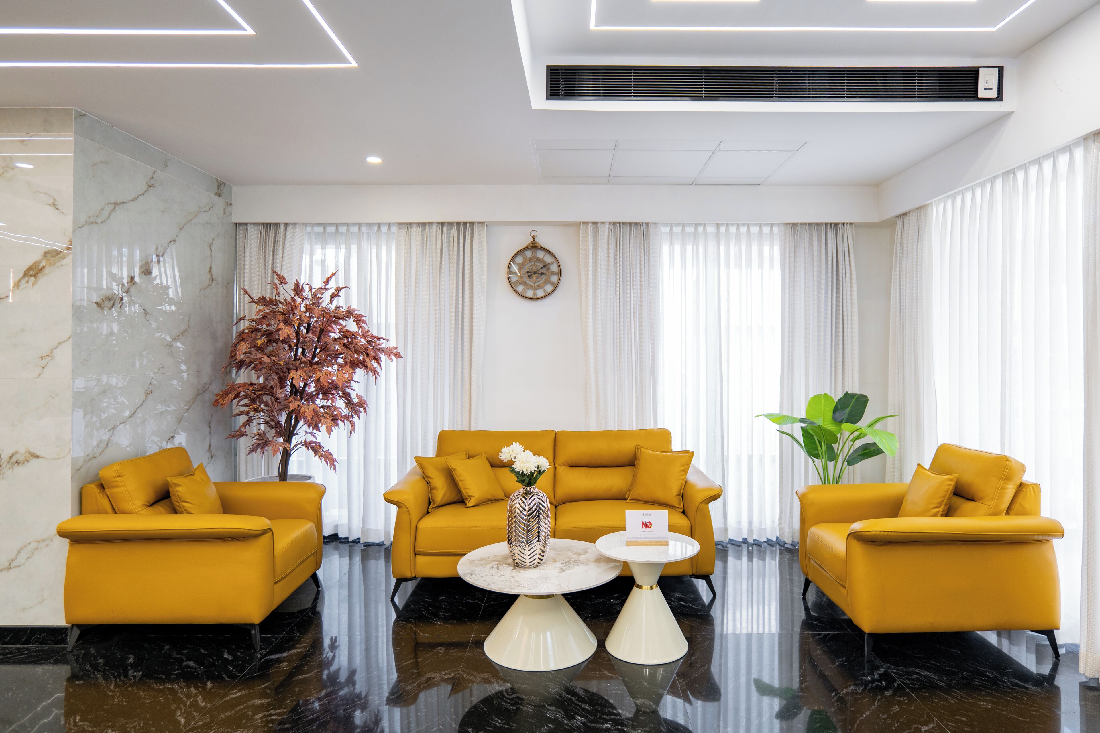 A modern hotel room with a marble wall, a yellow sofa set, a round coffee table, and a potted plant.