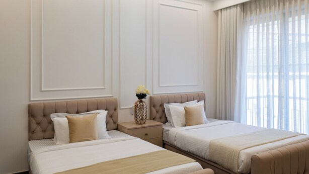 A hotel room with two beds, a decorative vase, and a large window with curtains. - ELIVAAS Nedumbally 4 BHK Villa (Ernakulam)