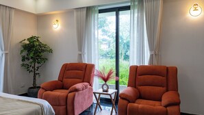 A room with two orange chairs, a bed, a potted plant, a small table with a vase, and a view of greenery through the window. - ELIVAAS Nedumbally 4 BHK Villa (Ernakulam)