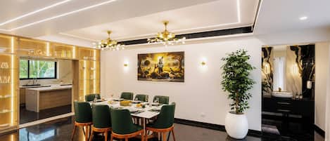 A modern dining area with a table set for six, green chairs, a large potted plant, and a painting on the wall.