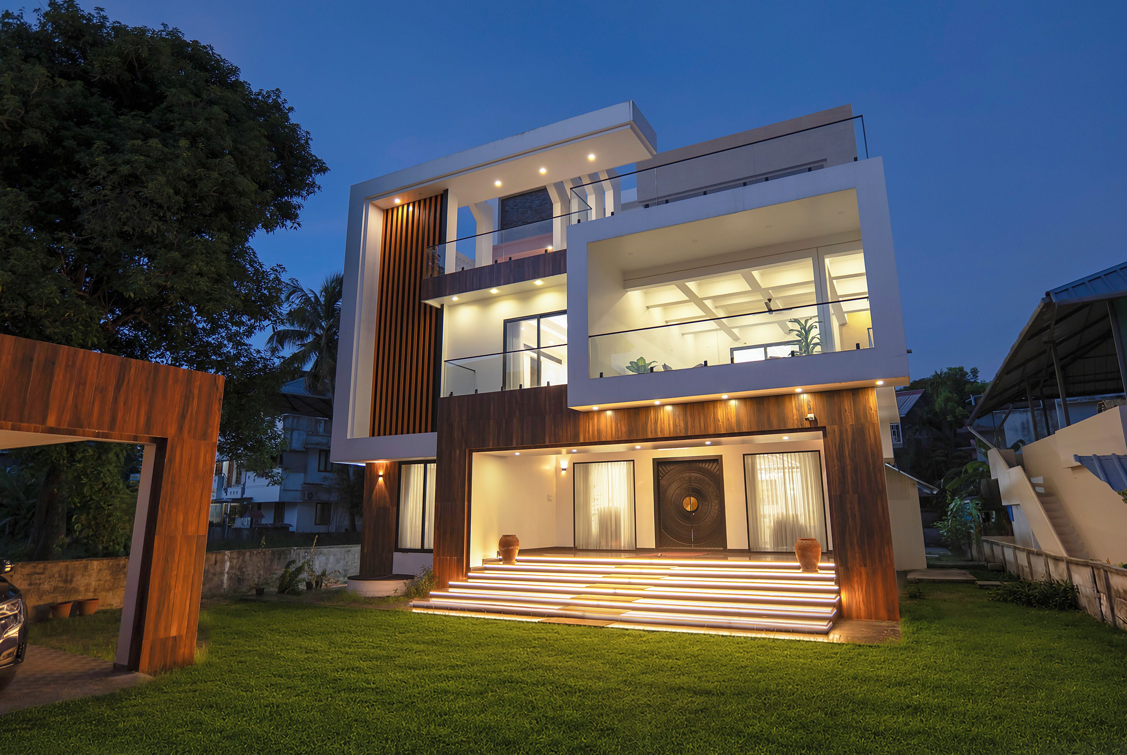Una casa moderna de dos pisos con balcón, ventanas amplias y una entrada bien iluminada.