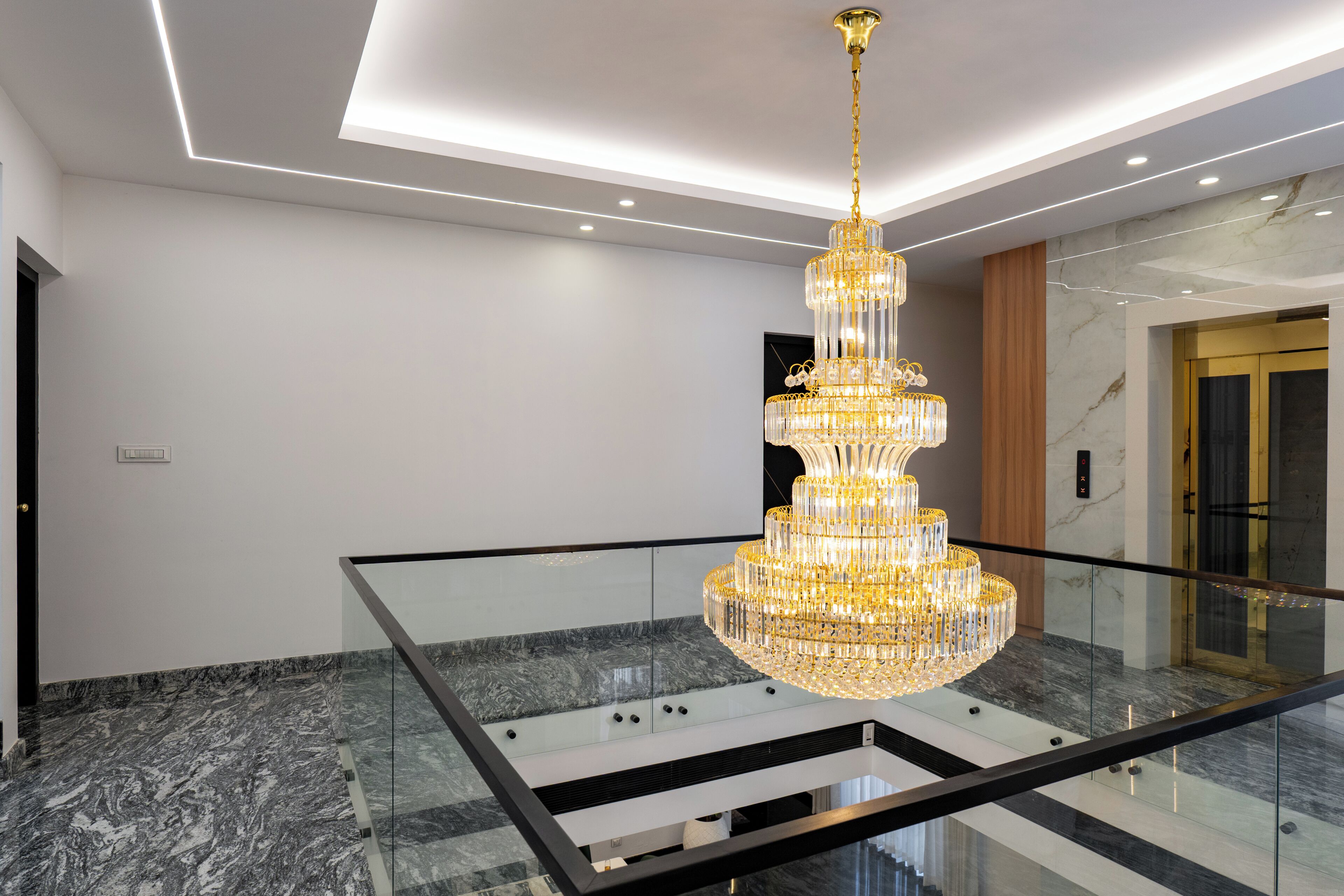 Un interior moderno con una gran lámpara de candelabro escalonada, barandilla de vidrio y suelo de mármol.
