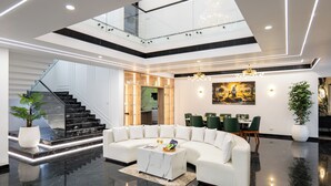 A modern interior with a white sectional sofa, a marble coffee table, a dining area with green chairs, and a staircase with glass railings. - ELIVAAS Nedumbally 4 BHK Villa (Ernakulam)