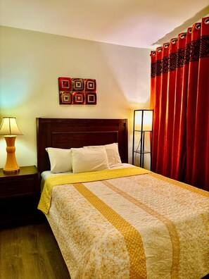 A hotel room with a bed, two bedside lamps, a nightstand, a headboard, and a red curtain.