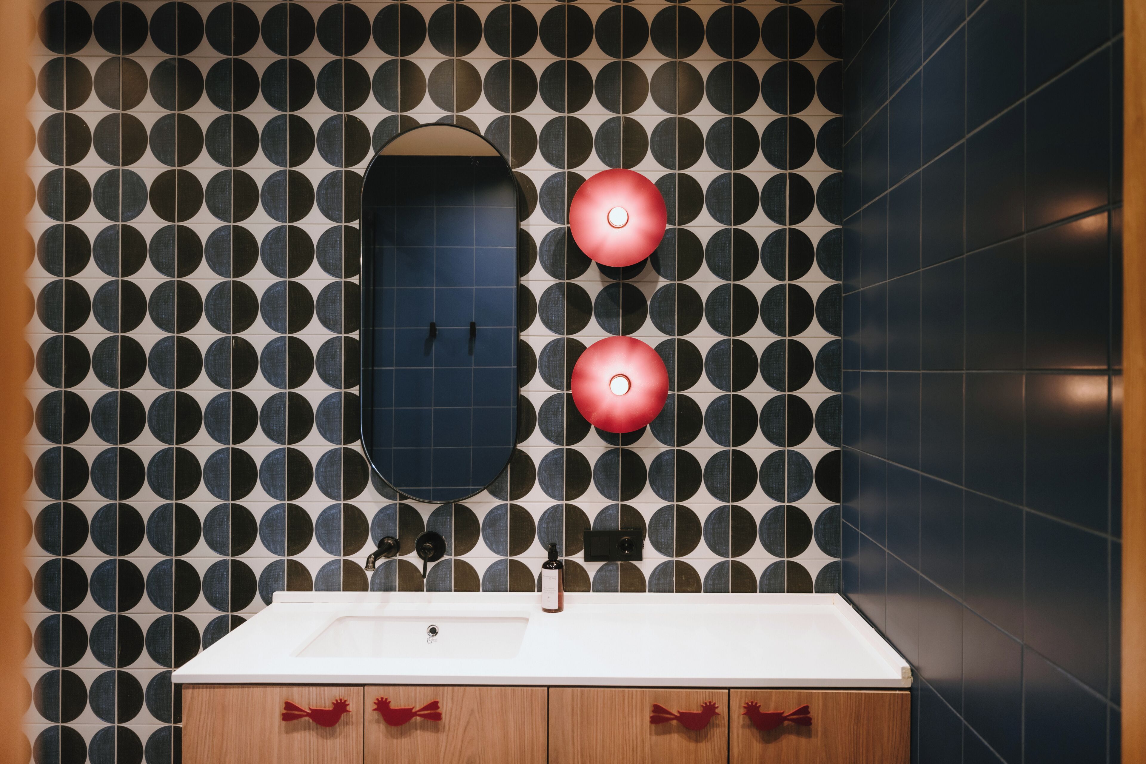 Ein Badezimmer mit Wandverkleidung, einem Spiegel, zwei roten Lampen, einem Waschbecken und Holzschränken.