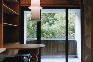 A room with a table, a chair, a hanging light fixture, and a large window with a view of trees.
