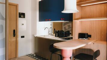 A compact kitchen with a wooden door, a white countertop, a black range hood, and a small dining area with two chairs.