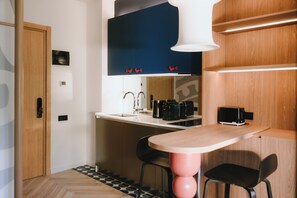 A compact kitchen with a wooden door, a white countertop, a black range hood, and a small dining area with two chairs. - Meidan Heritage Suites  (Tbilisi)