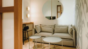 A minimalist living room with a sofa, two small tables, a round mirror, and a wooden chair.