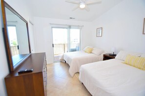 Quarto com duas camas, uma cômoda, um ventilador de teto e uma porta de vidro corrediça para uma varanda.