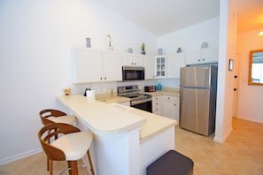 Eine moderne Küche mit weißen Schränken, Edelstahlgeräten, einer Bartheke und Holzbarhocker.