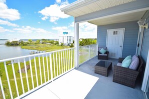 A covered balcony with wicker furniture, a white railing, and a view of a lake and buildings. - Oasis on the Bay 310 - Ocean City, MD (Ocean City)