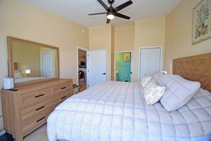 Ein Schlafzimmer mit Bett, Kommode, Deckenventilator und einer Tür zu einem anderen Raum.