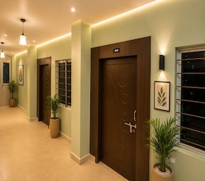 Un pasillo con puertas, plantas en macetas y lámparas fijadas a la pared.