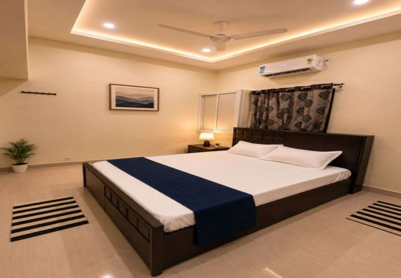 Une chambre moderne équipée d’un lit, d’une lampe de chevet, d’un climatiseur et d’un ventilateur de plafond.