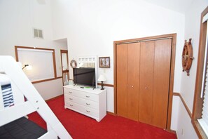 Une chambre avec une moquette rouge, une commode blanche avec un téléviseur, une armoire en bois et un élément de décoration murale en bois.