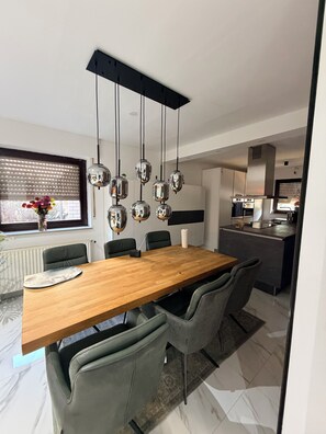 A modern dining area with a wooden table, grey upholstered chairs, and a hanging light fixture.