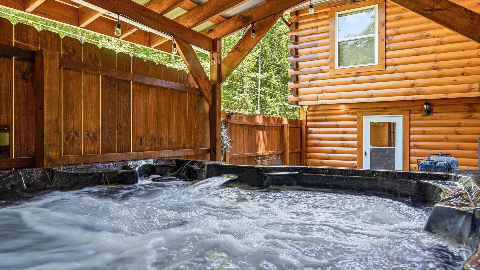 Eine Holzhütte mit Whirlpool, einer Holzterrasse und einem umzäunten Bereich.