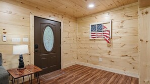 Ein Holzinnenraum mit einer braunen Tür, einem kleinen Tisch mit Lampe und einer amerikanischen Flagge an der Wand.